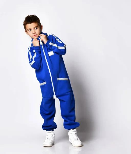 Niño vestido con un elegante chándal azul y zapatillas blancas posando sobre un fondo blanco. —  Fotos de Stock