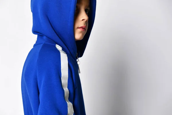 灰色の背景に暖かい青のジャンプスーツからフードに小さな男の子のクローズアップ. — ストック写真