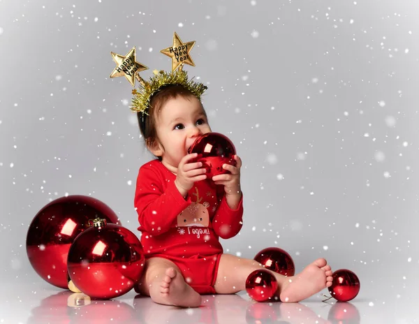 Small child wearing a headband with the inscription Merry Christmas on the floor indoors, surrounded by Christmas balls. First Christmas — Stock Photo, Image