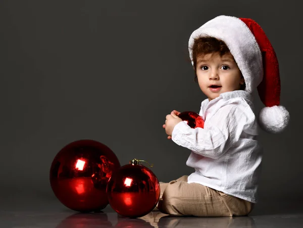 Mały chłopiec z kapeluszem Mikołaja i kulkami świątecznymi — Zdjęcie stockowe