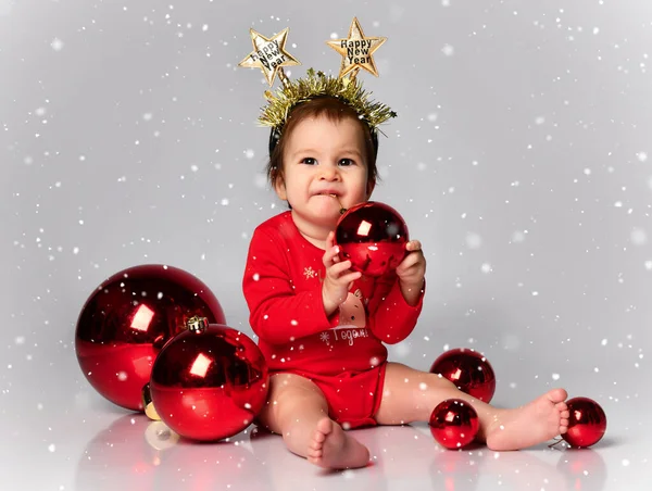 床にメリークリスマスの碑文が刻まれたヘッドバンドを身に着けている小さな子供は屋内で、クリスマスボールに囲まれています。第一クリスマス — ストック写真