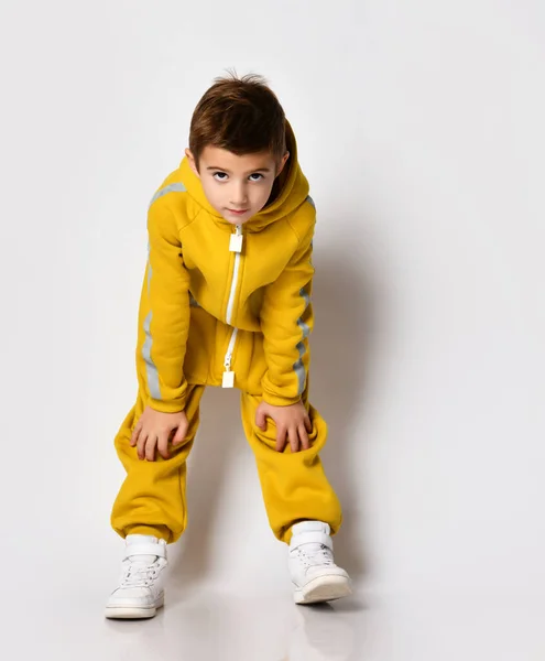 Chłopiec w żółtym kombinezonie dotykając kolana studio strzał — Zdjęcie stockowe