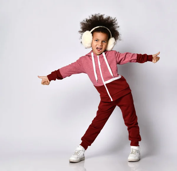African American girl sings and poses in warm headphones and sportswear.