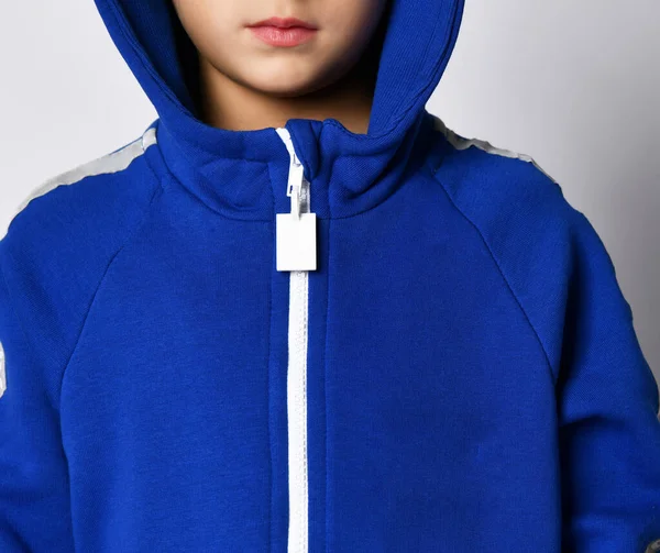 Acercamiento de un niño pequeño en una capucha de un mono azul cálido sobre un fondo gris. — Foto de Stock