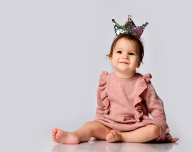 Taçlı saç bandı takmış şirin bir bebek gri arka planda oturuyor. Baba ve anne prenses.