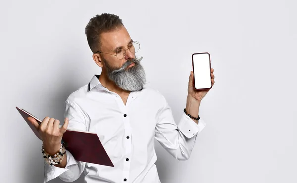 Uomo hipster in occhiali con notebook che mostra smartphone — Foto Stock