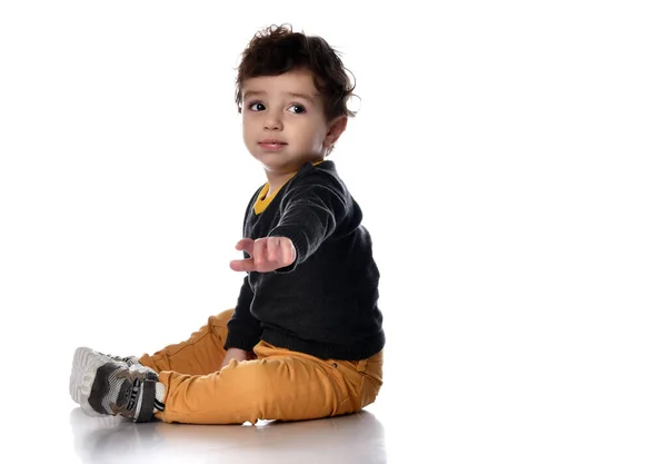 Mały chłopiec siedzi bokiem na białym tle i sięga do kamery patrząc w bok. — Zdjęcie stockowe