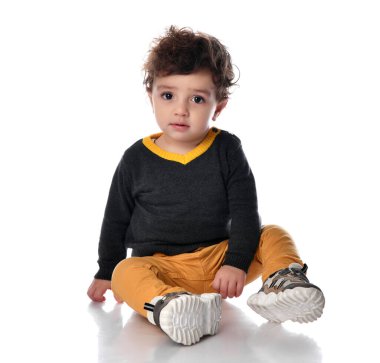 Beyaz arka planda oturan ve kameraya bakan kahverengi gözlü bir çocuğun portresi..