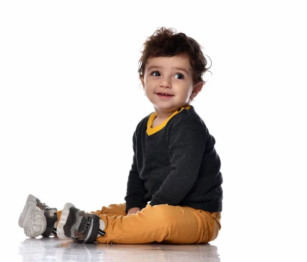 Enfant garçon en pantalon jaune assis latéralement sur le sol nous regardant sur un fond blanc avec de l'espace pour le texte libre — Photo