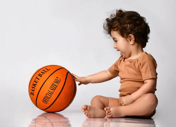 Μικρό αγόρι κάθεται ξυπόλητο και παίζει ένα νέο μπάσκετ σε γκρι φόντο. — Φωτογραφία Αρχείου