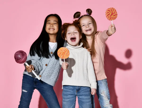Happy surprised children screaming and laughing posing with huge lollipop and spiral sweet candy studio shot portrait isolated on pink background. Funny crazy face expression and sugar addiction