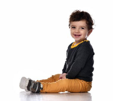 Beyaz arka planda oturan ve gülümseyen yakışıklı bir bebeğin yan görüntüsü..