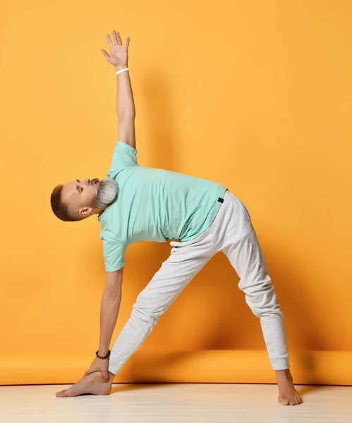 Gammal man stående på Utthita Trikonasana yogapose — Stockfoto