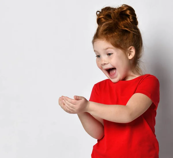 Aangenaam verrast roodharig meisje gelukkig kijkend naar iets in haar handpalmen. — Stockfoto