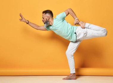 Sağlıklı sakallı bir adam tek bacağı üzerinde dengede duran portre geriyor.