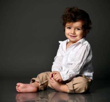 Şık bir erkek bebek yerde oturmuş, ayak portresiyle ilgileniyor.