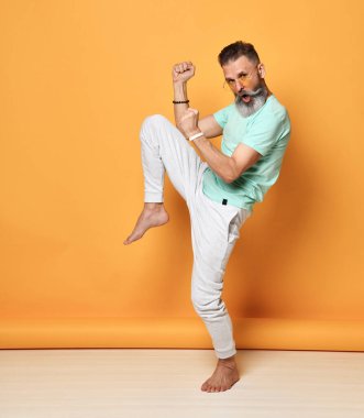 Modayı takip eden gri saçlı hippi dans ediyor ve parlak turuncu arka planda eğleniyor..