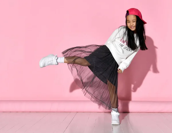 Πλευρική άποψη ενός μικρού κορεατικού μοντέλου κοριτσιού που ποζάρει στο στούντιο σε ροζ φόντο υψώνοντας το πόδι της. — Φωτογραφία Αρχείου