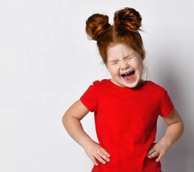 Kızıl saçlı ve çilli küçük kız ellerini belinde tutuyor ve yüksek sesle bağırıyor..