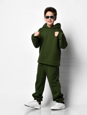 Havalı çocuk şık yeşil bir takım elbise, beyaz spor ayakkabı ve güneş gözlüğü takıyor..