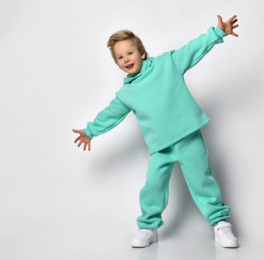 Gri bir arka planda kalın turkuaz takım elbiseli mutlu sarışın çocuk..