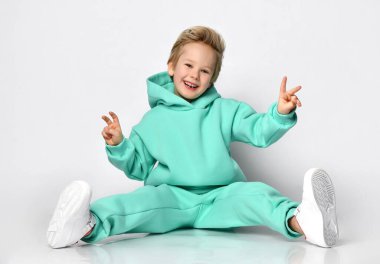 Sıcak spor takım elbiseli ve spor ayakkabılı oyuncu gri bir duvarın arkasında oturuyor..