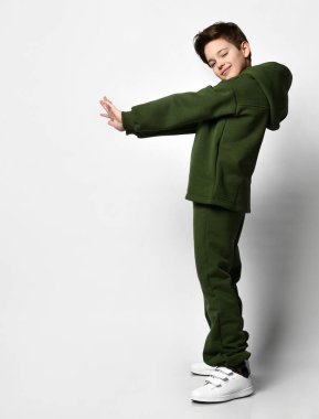 Sıcak spor kıyafetleri içinde genç bir çocuk gri arka planda durarak eğleniyor..