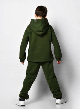 Küçük bir anaokulu öğrencisinin ya da okul çocuğunun kapüşonlu ve beyaz spor ayakkabılı sıcak yeşil eşofmanlı dikiz aynası. Gri arkaplan üzerinde kopyalama alanı ile izole.