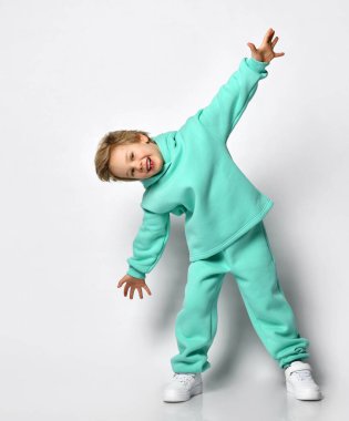 Gri bir arka planda kalın turkuaz takım elbiseli mutlu sarışın çocuk..