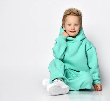 Turkuaz takım elbiseli çocuk gri bir duvarda yazı yazmak için boş alana yakın oturuyor..