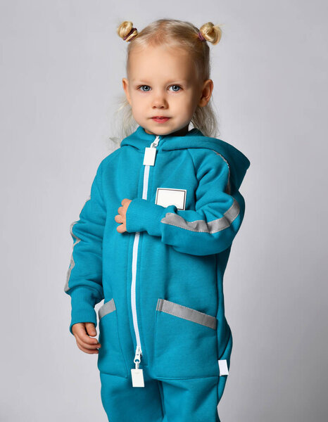 Маленькая дошкольница в тёплом синем спортивном комбинезоне на сером фоне.