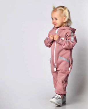 Sıcak, modaya uygun, pembe bir tulum giymiş küçük, sinsi sarışın kız..