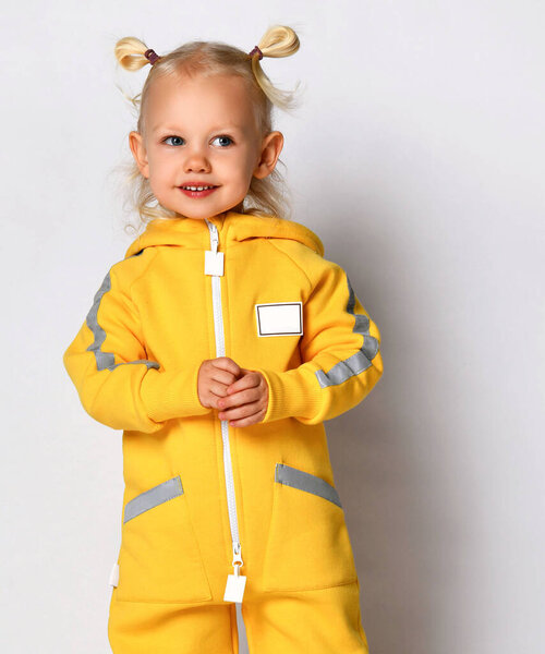 Портрет девочки в тёплом жёлтом спортивном комбинезоне на сером фоне.