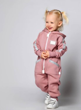 Sıcak, modaya uygun, pembe bir tulum giymiş küçük, sinsi sarışın kız..