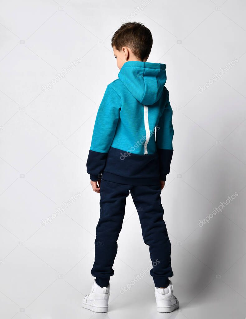 Kid in warm overalls, white sneakers walking along the studio wall. Full-length portrait. Childrens fashion, casual wear, comfortable children clothing for winter and autumn