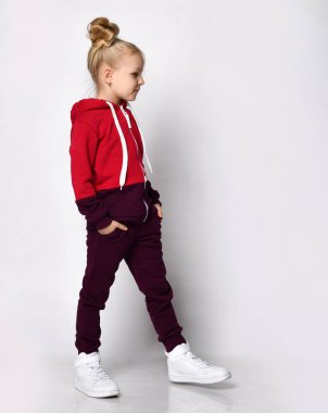 Sıcak tulumlu bir çocuk, stüdyo duvarında yürüyen beyaz ayakkabılı bir çocuk. Tam boy portre. Çocuk modası, günlük kıyafetler, kış ve sonbahar için rahat çocuk giysileri.