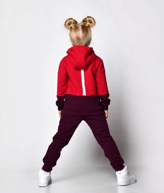 Ilık tulumlu, beyaz ayakkabılı, stüdyo duvarında yürüyen çocuk. Tam boy portre. Çocuk modası, günlük kıyafetler, kış ve sonbahar için rahat çocuk giysileri.