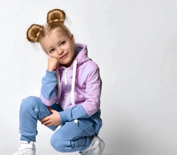 Menina loira bonito com penteados do pão na moda agachamento olhando para o espaço livre cópia. Infância, moda — Fotografia de Stock