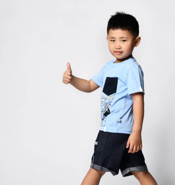 Yazlık tişörtlü ve şortlu Asyalı çocuk fotoğraf stüdyosu için poz veriyor.