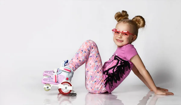 Schattig blond meisje in een roze trui en legendes gaat rolschaatsen. studio opname — Stockfoto