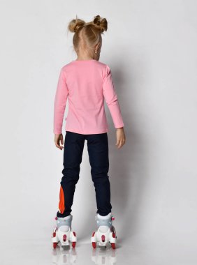 Beyaz stüdyo arka planında izole edilmiş, eğlencenin tadını çıkaran, paten kaymayı öğrenen tuhaf küçük bir kız. Mutlu çocukluk eğlence konsepti.