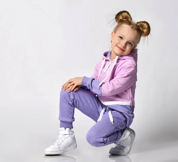 Cute blonde girl with trendy bun hairstyles squatting looking at the free copy space. Childhood, fashion Stock Image