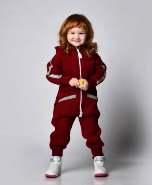 Oyuncak portresi olan, sıcak spor tulumlu, neşeli, kızıl saçlı küçük kız.