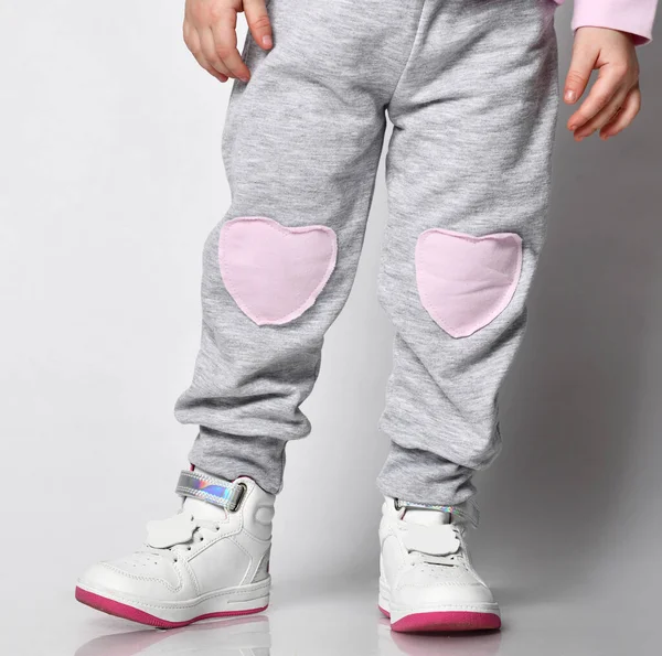 Gros plan d'un enfant en pantalon de sport gris avec une impression d'un visage de chat et des baskets blanches sur un fond gris. Premier plan — Photo