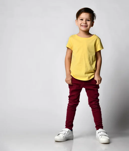 Portretul băiețelului preșcolar la modă în tricou galben, pantaloni din denim roșu, adidași albi, în picioare izolat pe fundal luminos — Fotografie, imagine de stoc