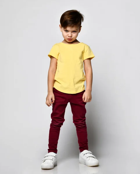 穿着黄色T恤、红色斜纹棉裤、白色运动鞋的学龄前时髦小男孩的肖像，在浅色背景下孤立无援 — 图库照片