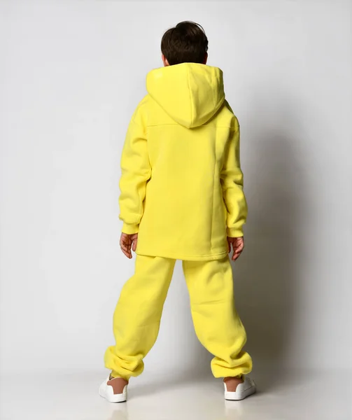 Vista trasera de un chico en un chándal amarillo brillante con una capucha, sobre un fondo claro —  Fotos de Stock