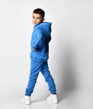 Mavi kapüşonlu, şık eşofmanlı bir çocuk. Kapüşonlu bir çocuk arkadan yarım dönüş gibi görünüyor. Beyaz tenli şık çocuk.,