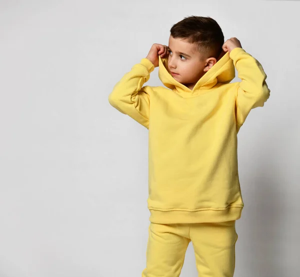 Smiling blond boy in a yellow tracksuit with a hood and trousers, white sneakers, isolated on white. Portrait of a child in cool clothes. Kids fashion, casual wear, comfortable kids wear —  Fotos de Stock