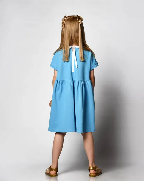 Ξανθιά σε ένα μοντέρνο γάμο μπλε γόνατο-length φόρεμα με ένα τόξο στο πίσω μέρος, πίσω όψη. καλοκαιρινή παιδική μόδα — Φωτογραφία Αρχείου